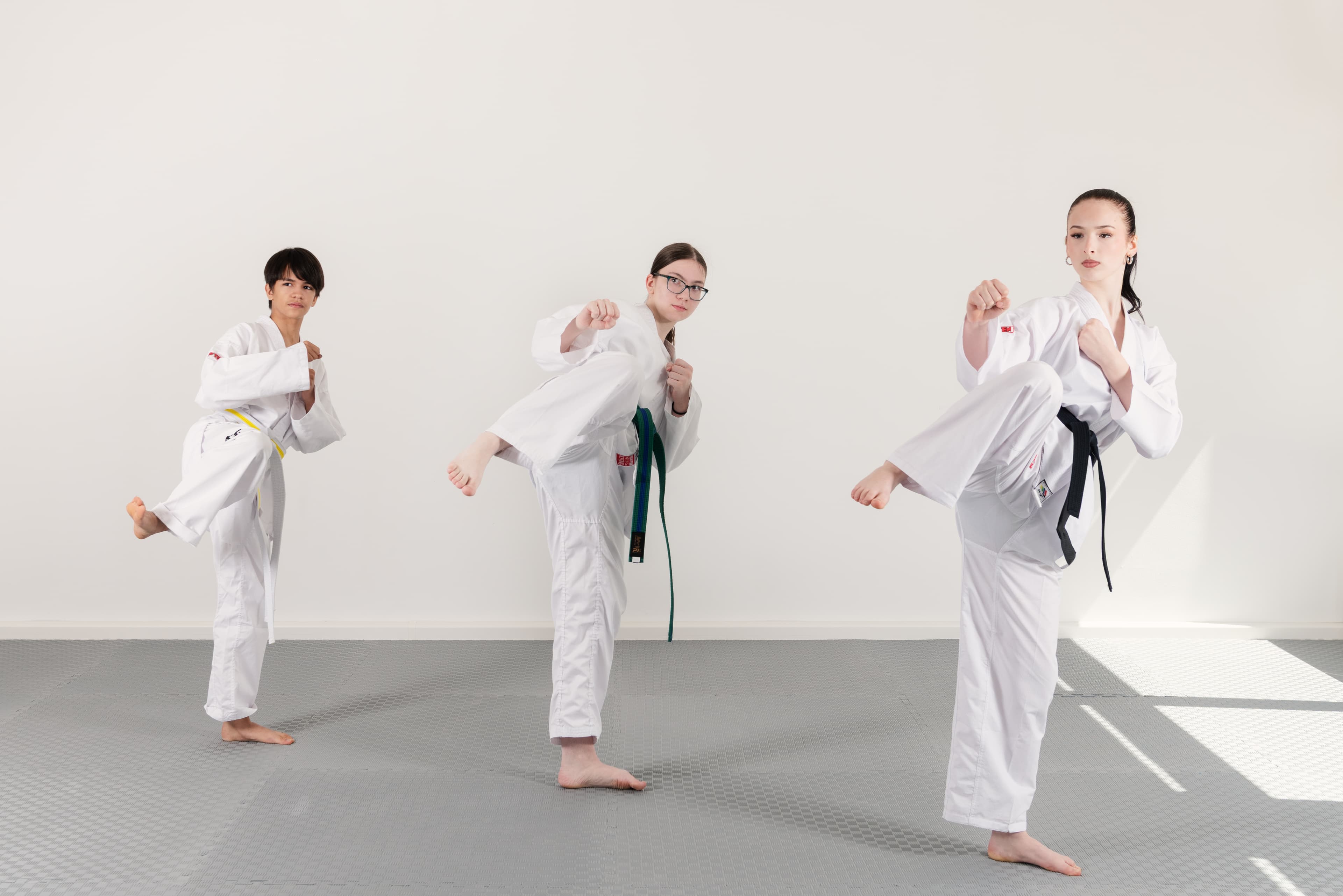 Drei Mitglieder zeigen Taekwon-Do-Techniken im Dojang.
